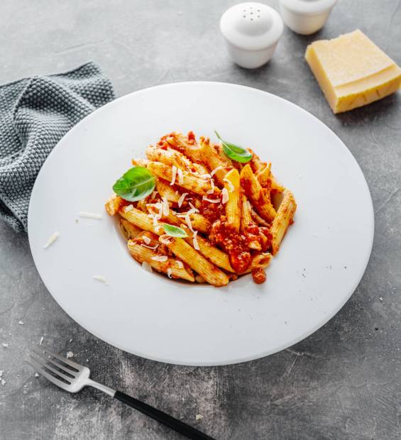 Tasty appetizing bolognese pasta penne with sauce and parmesan. Served on plate on grey background.  Closeup.
