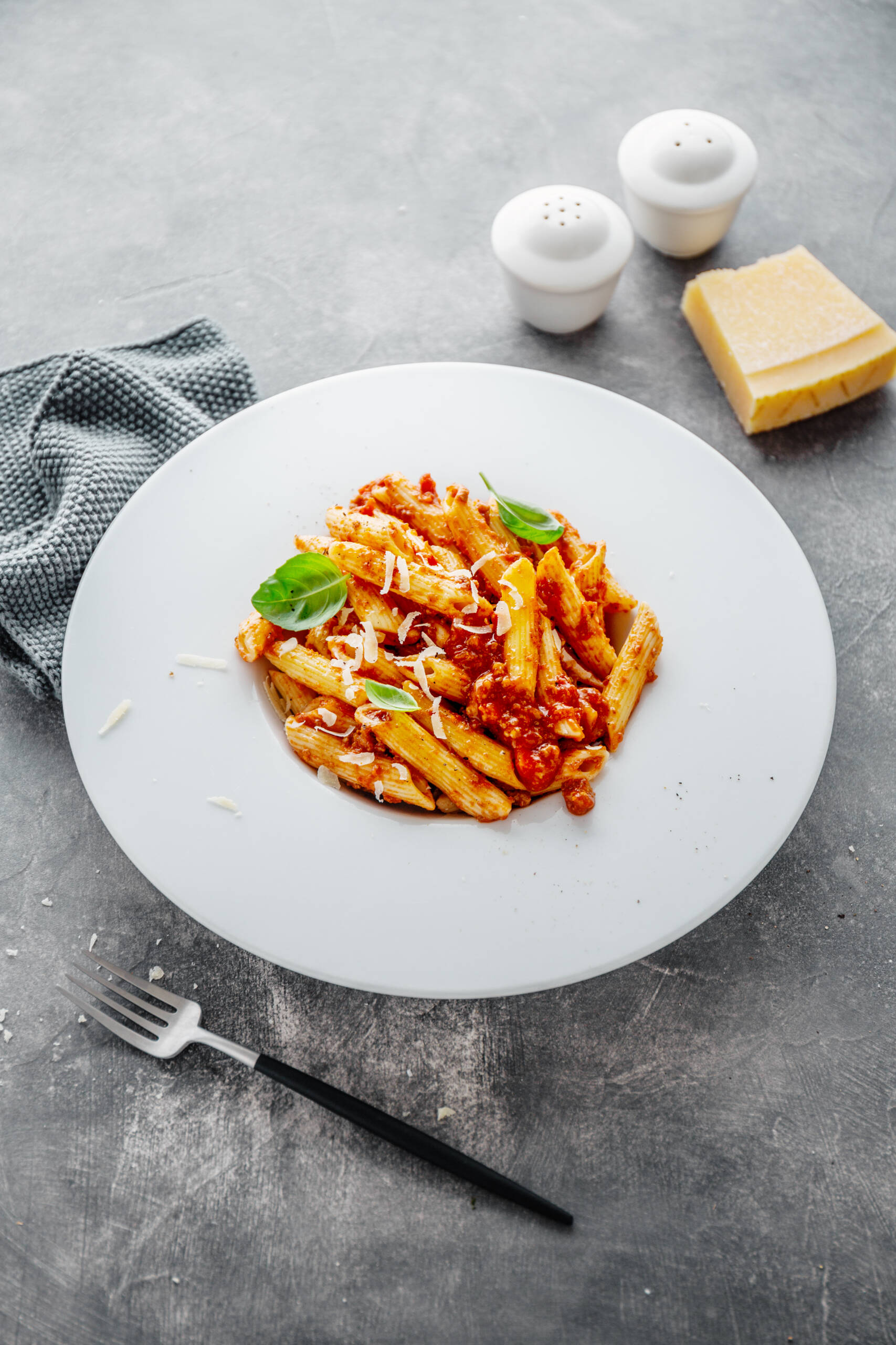 Tasty appetizing bolognese pasta penne with sauce and parmesan. Served on plate on grey background.  Closeup.